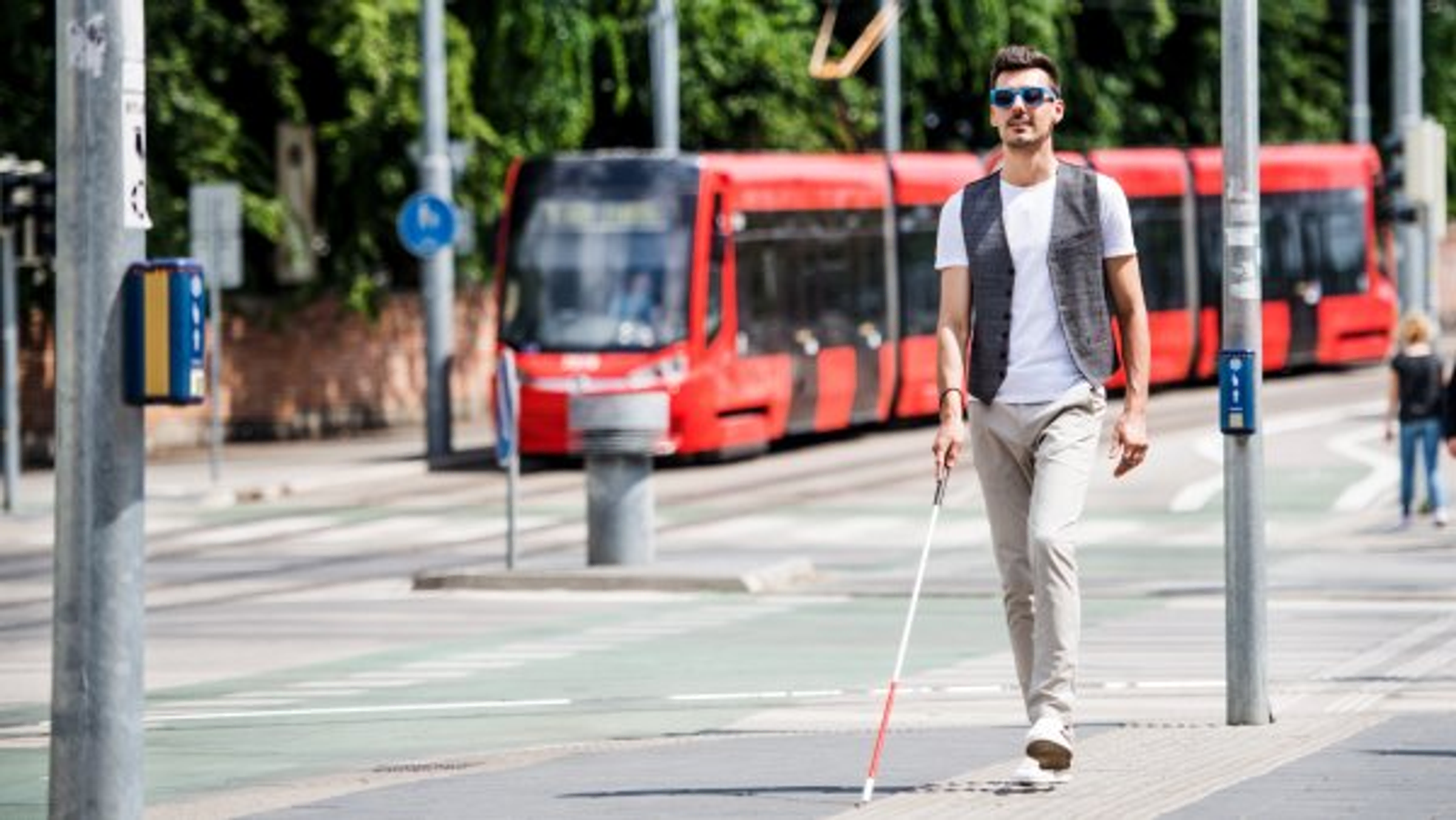 Muž se slepeckou holí jde po chodníku